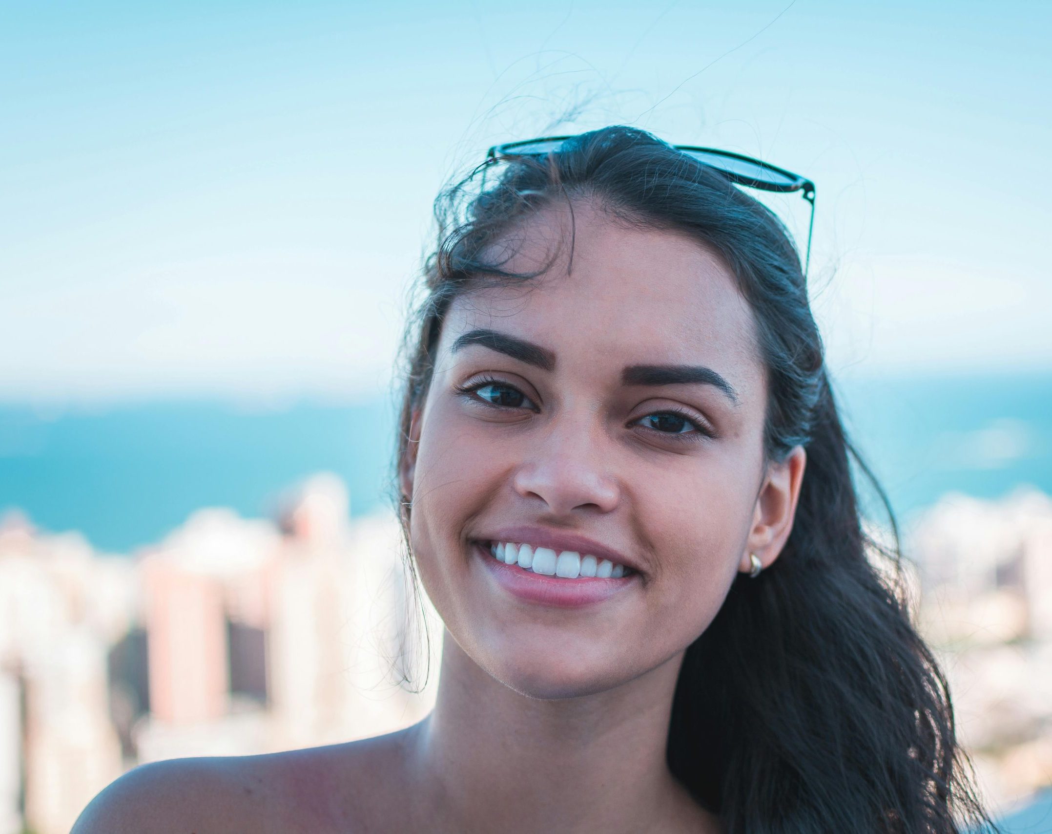 Portrait of a happy woman smiling with sunglasses on head, city skyline view.
